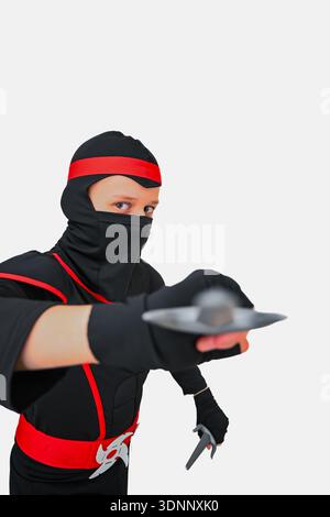 Enfant habillé comme un shuriken ninja visant dans la pose d'action avec un look concentré. Banque D'Images