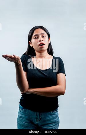 Jeune femme asiatique levant les yeux avec une expression confuse et douteuse, haussant les mains tout en se tenant debout sur un fond blanc de studio. Banque D'Images