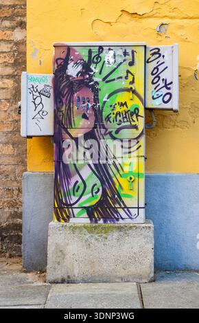 Graffiti coloré peint sur la boîte de service électrique contre le mur jaune texturé créant une scène urbaine dynamique de Street art Banque D'Images