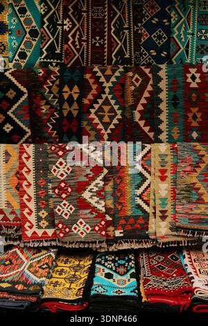 Tapis tissés traditionnels empilés avec des motifs géométriques colorés affichés à la vente. Textures textiles ethniques mettant en valeur l'artisanat régional et Banque D'Images