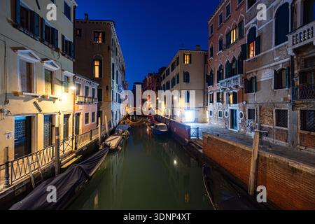 Découvrez le charme enchanteur de Venise alors que le crépuscule s'installe sur un canal tranquille bordé de bâtiments historiques. Les lumières chaudes se reflètent sur l'eau, highl Banque D'Images