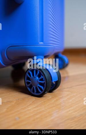 Gros plan de la roue bleue d'une valise moderne sur un plancher en bois, mettant en valeur un design élégant et une mobilité fluide. Idéal pour les concepts de voyage et de fonctionnalité Banque D'Images