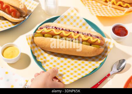 Un délicieux hot-dog garni de moutarde, d'oignons hachés et de cornichons servis sur un petit pain. Présenté sur une assiette avec des condiments d'accompagnement, présentant un classique Banque D'Images