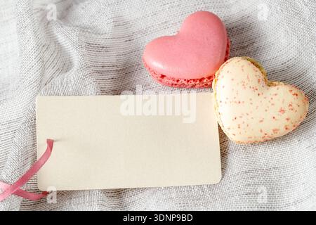 Carte de Saint-Valentin vide ou étiquette vierge pour le texte et deux macarons en forme de coeur sur fond textile gris clair. Biscuits français avec râpe Banque D'Images