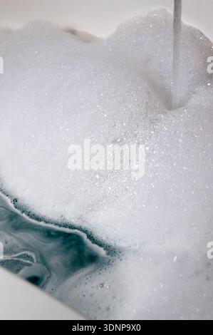 Bulles de savon mousseuses couvrant l'eau dans un évier de cuisine pendant qu'il se remplit, prêt pour laver la vaisselle à la main et les tâches de nettoyage ménager. Banque D'Images