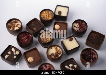gros plan studio de chocolats artisanaux assortis et pralines sur une table blanche, mettant en vedette des ganaches noires, au lait et blanches avec des noisettes et du café Banque D'Images