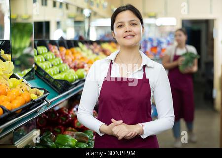 Jeune femme vendeuse en uniforme posant dans l'épicerie Banque D'Images
