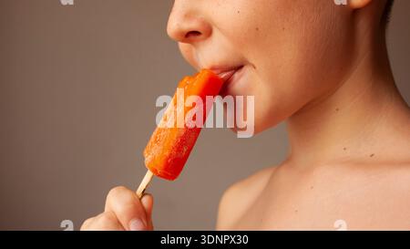 Un enfant mange de la crème glacée à la sucette orange, photo verticale. Banque D'Images