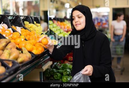 Une jeune femme en hijab achète des mandarines à l'épicerie Banque D'Images