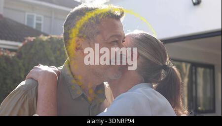 Embrassant couple mature tenant près du porche avant, homme en chemise légère, poudre jaune Banque D'Images
