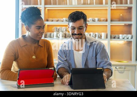 Divers collègues d'affaires collaborant et examinant le contenu sur des tablettes numériques pendant une pause, discutant des idées dans une cuisine confortable de coworking Banque D'Images
