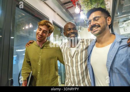 Collègues masculins multi ethniques marchant et riant dans un espace de coworking moderne, partageant un moment convivial de collaboration et un cultu positif sur le lieu de travail Banque D'Images