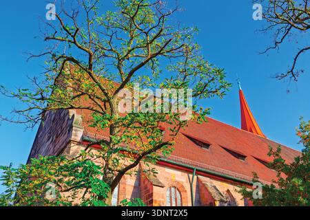 Médiévale : Jakob Church à Nuremberg, Allemagne, encadrée par des branches d'arbres feuillus contre un ciel clair. Toit en tuiles rouges et tour de beffroi pointu sont promin Banque D'Images