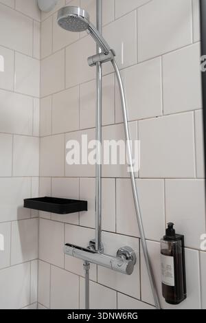 Vue détaillée d'un système de douche chromé moderne, comprenant une tête réglable, une étagère noire, un distributeur de savon et des carreaux de métro blancs, mettant en valeur le contempo Banque D'Images