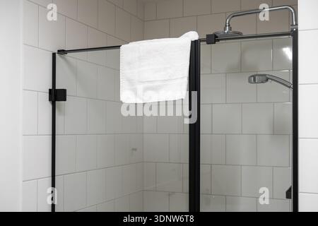 Vue détaillée d'une douche de salle de bains élégante, présentant des carreaux de métro blancs, une serviette propre, et des pommes de douche modernes de tête et de main pour la rénovation Banque D'Images