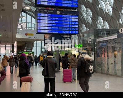 Poznan, Pologne - 30 novembre 2025 : à l'intérieur d'une gare moderne animée, les voyageurs avec des bagages sous des panneaux d'arrivée numériques lumineux, Biedronka et Za Banque D'Images
