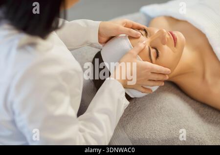 Esthéticienne faisant un massage facial relaxant en appliquant une pression douce sur les muscles faciaux de la femme Banque D'Images