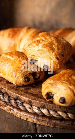 Croissants au chocolat fraîchement cuits disposés sur un plateau rustique en bois aux tons chauds Banque D'Images