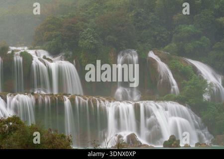La cascade de Ban Gioc coule sur de larges falaises calcaires étagées dans de multiples ruisseaux en forme de rideaux, entourés d'une forêt dense. Banque D'Images