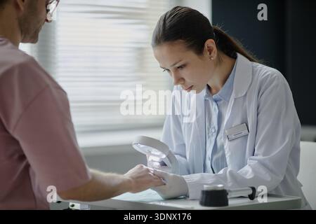 Dermatologue femme caucasienne jeune adulte examinant la peau de la main d'un patient masculin Banque D'Images