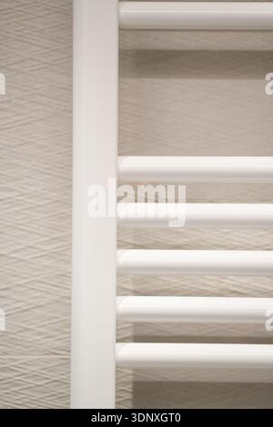 Radiateur de serviettes blanches installé sur un mur beige clair texturé dans une salle de bain moderne, offrant chaleur et solution de séchage pratique Banque D'Images