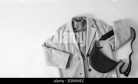 Style monochrome. Manteau ou veste en laine gris clair, pull en cachemire gris foncé et sac en cuir noir isolé sur fond de tissu neutre. Automne Banque D'Images