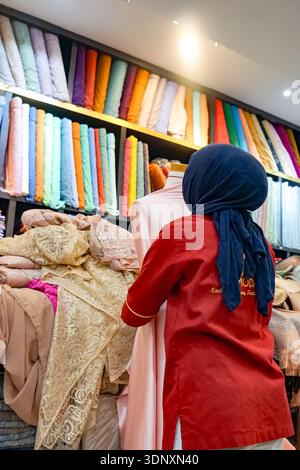 Batam, Indonésie, 1er février 2026 : personne ajustant le tissu sur mannequin dans le magasin de textile avec des rouleaux de tissu coloré. Banque D'Images