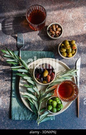 Vue de dessus d'une table rustique avec un assortiment d'olives grecques et de vin ambré. Des bols avec des olives vertes et noires sont disposés élégamment sur un textu Banque D'Images