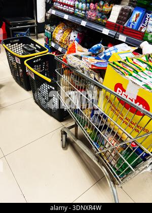 Lviv, Ukraine - 07 février 2026 : allée lumineuse du magasin avec un chariot et des sacs de collations et d'épicerie à proximité. Banque D'Images