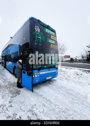 Lviv, Ukraine - 07 février 2026 : bus à impériale bleu attend dans un terrain enneigé comme un passager embarque. Banque D'Images