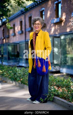 Une femme d'affaires souriante dans une veste jaune éclatante et un Jean élégant se tient à l'extérieur, exsudant confiance et joie. Son comportement joyeux illumine le d. Banque D'Images