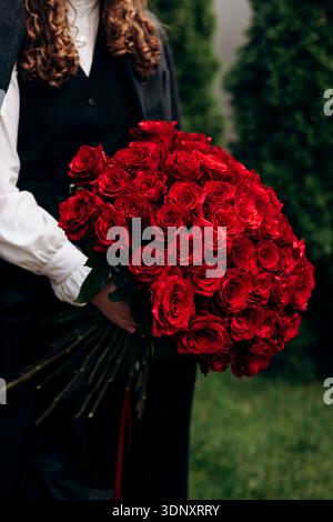 Une femme aux cheveux bouclés tient un magnifique bouquet de roses rouges éclatantes. Les fleurs sont fraîches, luxuriantes et magnifiquement disposées, créant un cont frappant Banque D'Images
