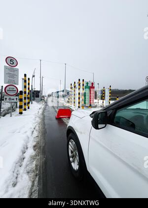 Hrebenne, Pologne - 07 février 2026 : poste de contrôle frontalier polonais ukrainien enneigé avec une voiture blanche, des postes à rayures noires jaunes et de nombreux panneaux le long du Banque D'Images