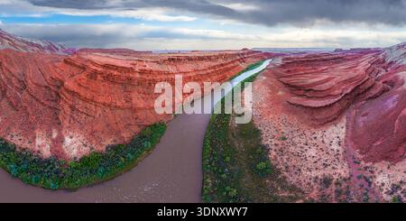 Une vue aérienne époustouflante capture les formations rocheuses rouges vibrantes et la rivière sinueuse du canyon Rio San Juan dans l'Utah, aux États-Unis, avec un ciel spectaculaire au-dessus d'un Banque D'Images