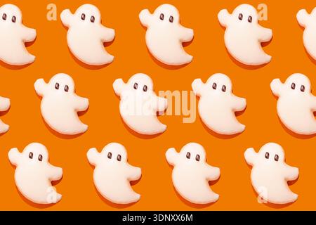 Adorables biscuits en forme de fantôme avec glaçage blanc décorent un fond orange. Parfaites pour les fêtes d'Halloween, ces douces friandises ajoutent une touche ludique à votre tenue Banque D'Images