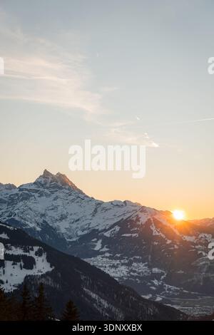 Une vue imprenable sur les Alpes suisses, couvertes de neige, avec un lever de soleil brillant projetant une lueur chaude. La scène hivernale capture la beauté froide et sereine Banque D'Images
