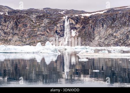 Magnifique paysage du Groenland avec une cascade majestueuse descendant des falaises escarpées dans des eaux glacées, entouré de neige et de formations de glace Banque D'Images