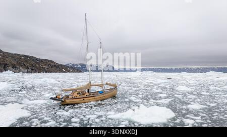 Un voilier solitaire navigue dans les eaux glacées du détroit de Davis, au Groenland, entouré d'icebergs flottants. La scène tranquille capture la beauté brutale Banque D'Images