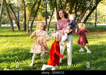 Une mère joyeuse et ses filles profitent d'une journée ensoleillée au parc, jouant et se liant au milieu des arbres verts et de l'herbe, créant ainsi des souvenirs de famille durables Banque D'Images