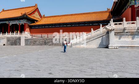 Une femme explore la Cité interdite historique de Pékin, en Chine, avec ses murs rouges emblématiques, ses toits en tuiles orange et ses détails architecturaux ornés sur un s. Banque D'Images