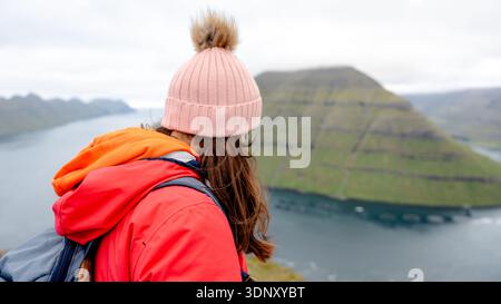 Vue arrière d'une femme méconnaissable profitant de la vue imprenable sur l'île de Kunoy et l'île de Kalsoy d'un côté, du sommet de la montagne Klakkur sur Bordoy Banque D'Images