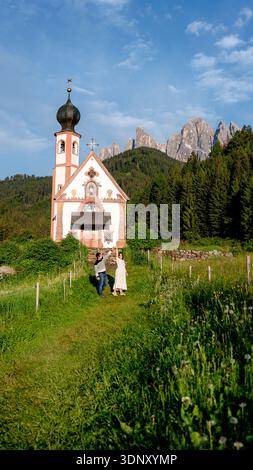 Un couple se tient devant la charmante Chiesetta di San Giovanni a Ranui, située dans le Val di Funes, avec les superbes montagnes de la chaîne Odle dans l'arrière-pays Banque D'Images