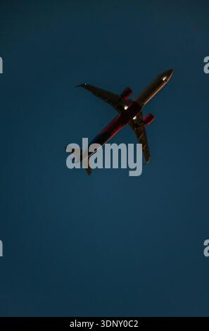 Silhouette d'un avion commercial volant au-dessus de Lisbonne au coucher du soleil, avec un ciel clair et sombre comme toile de fond. L'image capture l'élégance et la majesté Banque D'Images