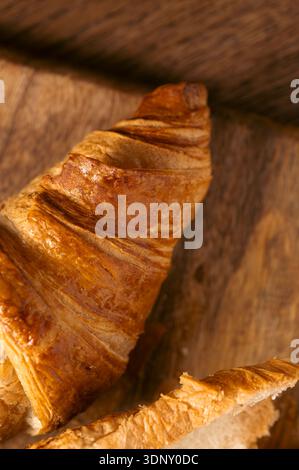 Un croissant brun doré présente des couches feuilletées et une texture beurrée, sur une table en bois rustique. Parfaitement cuit, il incarne l'essence de l'artisan Banque D'Images