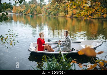 Un couple aimant profite d'un moment paisible dans un parc d'automne, ramant sur un lac tranquille entouré de feuillage d'automne vibrant, créant un pittoresque et R Banque D'Images