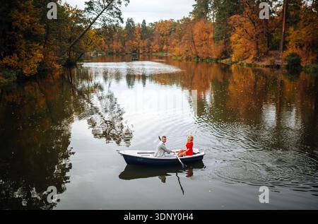 Un couple aimant profite d'une promenade sereine en bateau entouré d'un feuillage d'automne vibrant dans un cadre paisible de parc, créant une atmosphère romantique et tranquille Banque D'Images