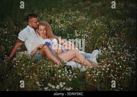 Un couple attendu profite d'un moment serein dans un pré, entouré de fleurs sauvages. La scène capte leur amour et leur anticipation, reflétant l'harmonie Banque D'Images