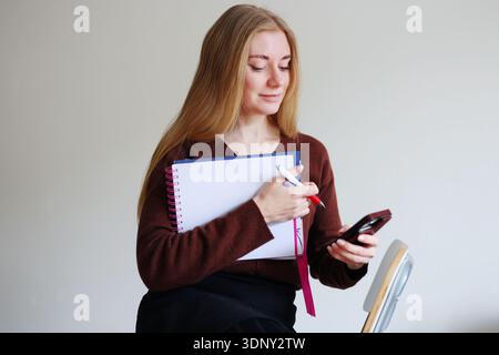 Femme tenant un cahier et vérifiant le smartphone. Concept de productivité et de planification avec style de vie moderne et espace de copie. Banque D'Images