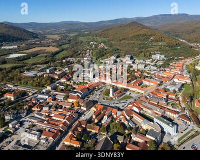Vue aérienne des toits en terre cuite descendant jusqu'à la place de la ville, dominée par l'emblématique tour blanche et ombragée par les collines boisées lointaines, Banque D'Images