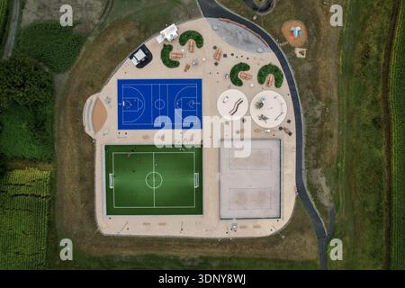 Vue aérienne d'un terrain de basket-ball bleu vibrant, d'un terrain de football vert et d'un terrain de volley-ball de sable au milieu d'une végétation luxuriante, Monthey, Valais, Suisse. Banque D'Images